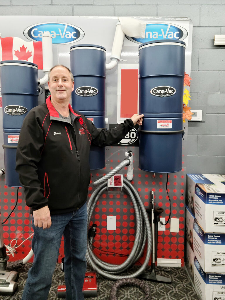 Steve Pond, Owner of Elmira Vacuum, stands next to Cana-Vac central vacuums, providing small town service